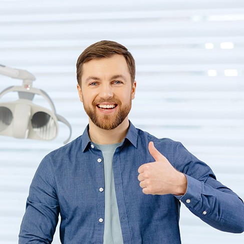 Bearded man in dental office giving thumbs up and smiling