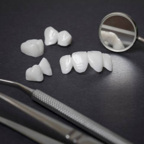 Several white dental crowns and fillings on table with dental instruments