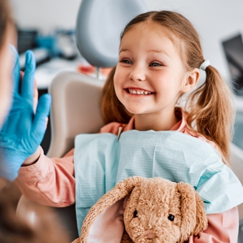 Young girl in dental chair giving dentist a high five